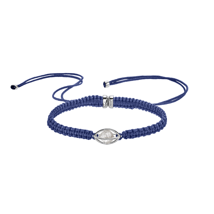 Leo Wittwer Armband Rough Cut - Ein goldener Käfig in dessen inneren ein ungeschliffener weißer Brillant sitzt. Der Käfig wird an den Seiten von zwei Makramee Bänder in blau gehalten.